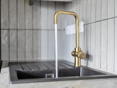 A sink with a gold faucet dispensing water at a kitchen