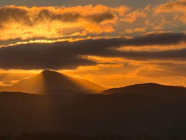 A mountain silhouette against a sunset with clouds in the sky