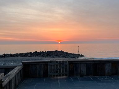 A sunset over the sea with rocks and a gate at Y Glyn in Borth