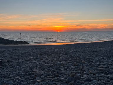 A sunset over the ocean with pebbles in the foreground at a beach