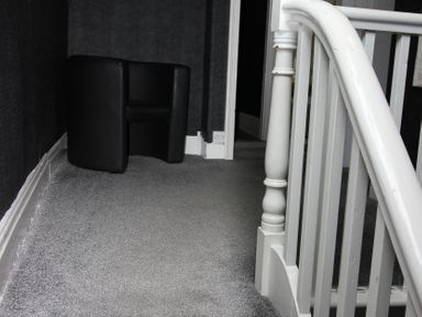 A hallway with a black chair and staircase at Cornerhouse Apartment 1 in Llandudno