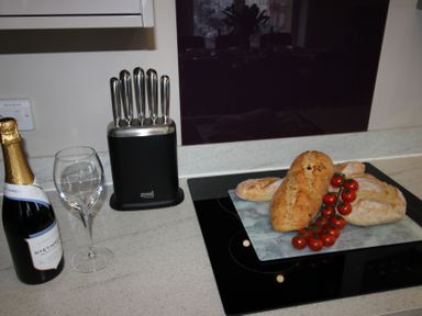 A kitchen with a wine bottle, glass, knife block, bread, and cherry tomatoes at Cornerhouse Apartment 2 Llandudno