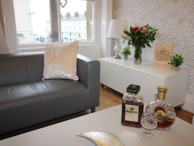 A living room with a sofa, coffee table, flowers, and decorative items at Cornerhouse Apartment 3 in Llandudno
