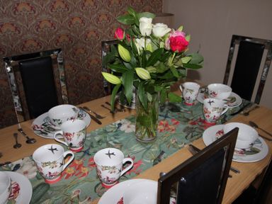 A dining table set with plates and cups along with flowers at Cornerhouse Apartment 5 Llandudno