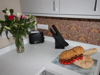 A kitchen with flowers, a toaster, knife block, bread, and tomatoes at Cornerhouse Apartment 5 Llandudno