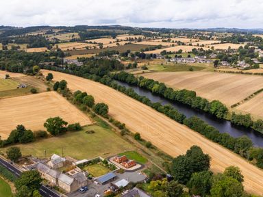 An aerial view of fields, river, trees, and houses at 2 West Dunkirk Neuk in Humshaugh