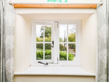 A window with curtains overlooking greenery at The Cheese House near Charmouth
