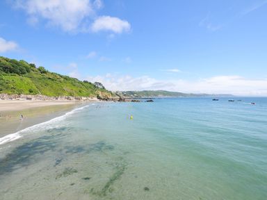 A beach with people swimming and boats at The Cheese House near Charmouth