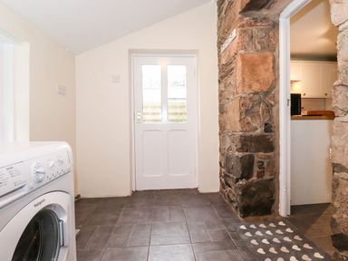 A laundry room with a washing machine and stone wall at Irt Cottage Seascale