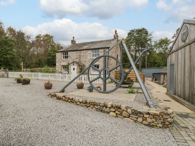 An outdoor area with a stone house and mechanical wheel at Irt Cottage in Seascale