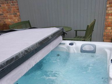 A hot tub with cover near a table and chair at 3 Bedroom Cottage Hot Tub Garden Parking Dunkeswell