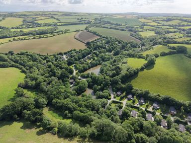 An aerial view of fields and houses around a lake at 5 Tree Tops in Dobwalls