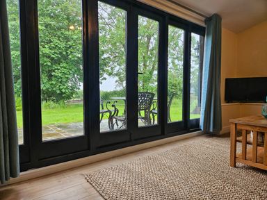 A living room with glass doors leading to outdoor furniture at Lily's Cottage Suffolk Sleeps 2 with Pets Mendlesham Green near Stowmarket