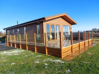 A lodge with decking and outdoor chairs at 2 Bedroom Sleeps 4 Lodge Smart Tv Hot tub Dogs Ok near Lochwinnoch
