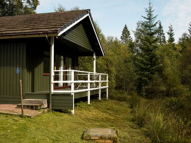 A lodge with a deck and outdoor seating near trees at 2 bedroom lodge with free WiFi and mountain view near Crianlarich