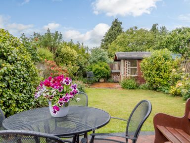 A garden with a metal table and chairs and a flower pot on the table a lawn and a wooden shed at Hollyhedge Cottage in Briston