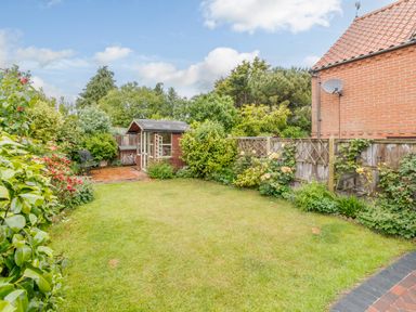 A garden with grass lawn wooden shed bench and plants along a fence at Hollyhedge Cottage in Briston