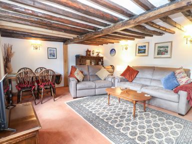 A living room with a sofa, coffee table, and dining table at Hollyhedge Cottage in Briston