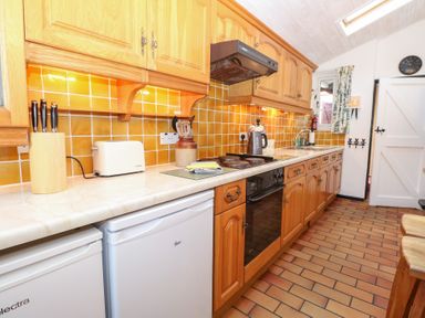A kitchen with wooden cabinets and appliances at Hollyhedge Cottage in Briston