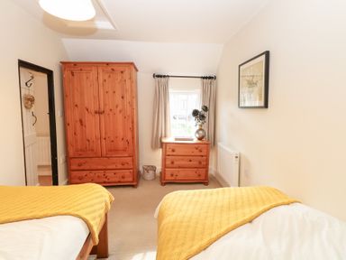 A bedroom with two beds and wooden furniture at Hollyhedge Cottage in Briston