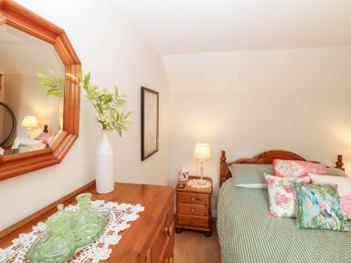 A bedroom with a bed, dresser, and mirror at Hollyhedge Cottage in Briston