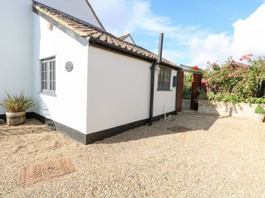 An exterior view of a cottage with a gravel path at Hollyhedge Cottage in Briston