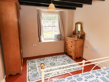 A bedroom with a wardrobe, window, rug, and dresser at Felin Bach in Aberdaron