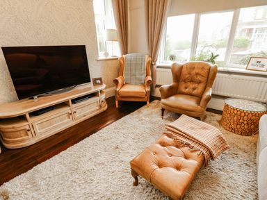A living room with a television, two armchairs, and a coffee table at 11 Bryn Goleu Avenue North in Holyhead