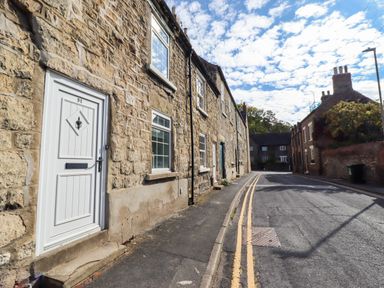 An outdoor street with stone buildings and a door at Blue Cottage in Malton