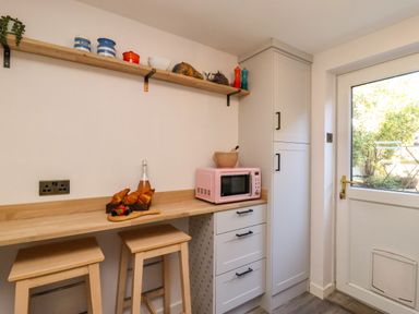 A kitchen with a pink microwave and bar stools at Blue Cottage Malton