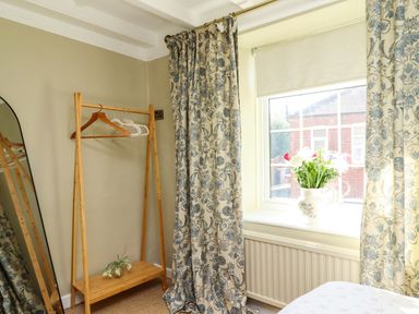 A bedroom with a mirror, curtains and a window at Blue Cottage in Malton