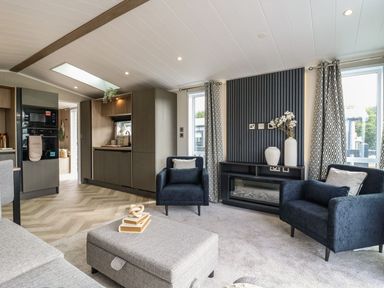 A living room with a sofa and armchairs connected to kitchen cabinets at Lakewood Plot 7 in Clacton-on-Sea