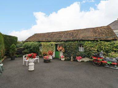 A garden area with a thatched roof building and flower pots at Teresa's Cottage