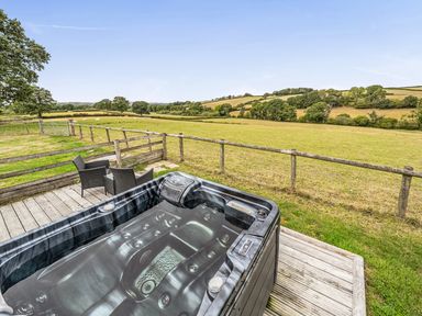An outdoor space with a hot tub and chairs overlooking a field at The Shippon, Breathtaking Views, Private Hot Tub in Winkleigh