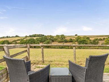 A seating area with chairs and a table overlooking a field at The Shippon, Breathtaking Views, Private Hot Tub in Winkleigh