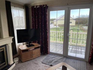 A living room with a television and door leading to the deck at Chalet Sleeps 4 Near Cymyran Beach Caergeiliog