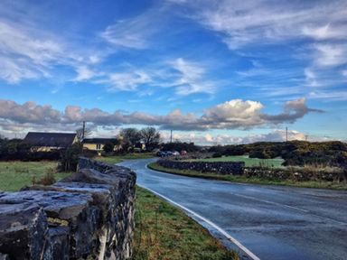 A winding road alongside a stone wall with houses in the distance at Chalet Sleeps 4 Near Cymyran Beach Caergeiliog