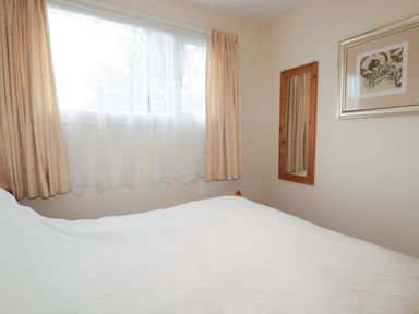 A bedroom with a bed, window, curtains, mirror, and picture at Villa 12 near Camelford