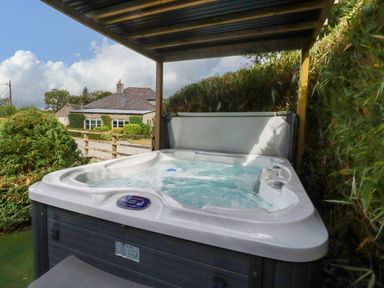 A hot tub under a wooden shelter at Honey Bee Bus in Menheniot