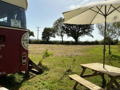 An outdoor area with a red bus, table, and umbrella at Honey Bus in Menheniot