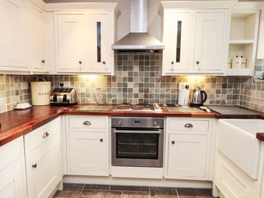A kitchen with cabinets, oven, sink, and appliances at 2 bed Criccieth