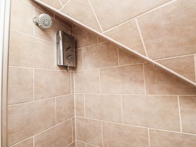 A shower with tile wall and showerhead at 2 bed Criccieth