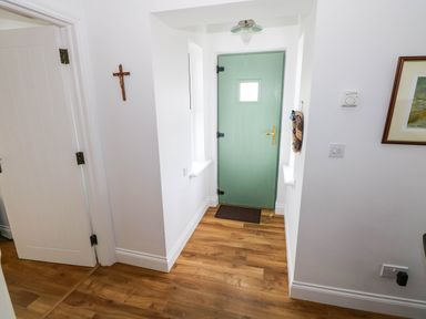 A hallway with a green door and wooden flooring at Doughbeg Beach Cottage