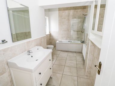 A bathroom with a sink, bathtub, toilet and mirror at Doughbeg Beach Cottage