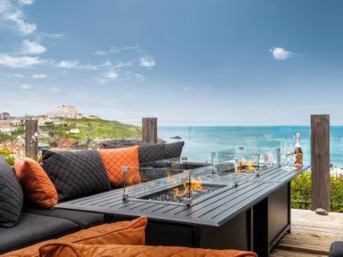An outdoor seating area with fire table and cushions at By The Sea in Newquay