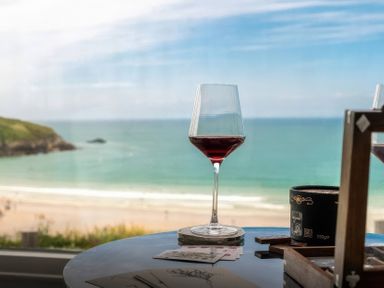 A glass of red wine on a table with postcards and a candle at By The Sea in Newquay