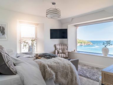 A bedroom with a tv and a window overlooking the sea at By The Sea in Newquay