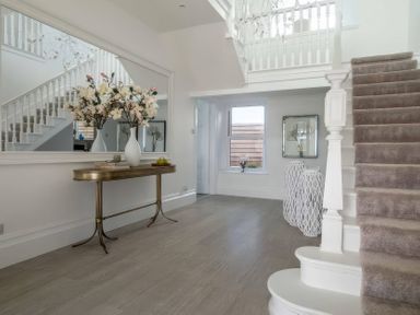 A hallway with a staircase and flowers on a table at By The Sea in Newquay