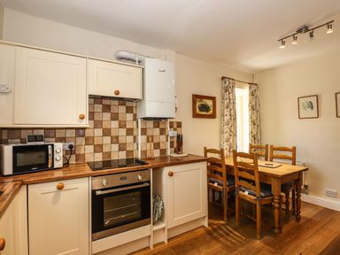 A kitchen with cabinets and a dining table at Jessicas Cottage in Windermere