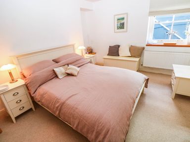 A bedroom with a bed, nightstand, lamp, and window at Basement Apartment in Tenby